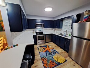 A modern kitchen with dark blue cabinets, stainless steel appliances, and a colorful rug.