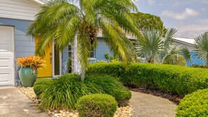 A house with a yellow door, surrounded by well-maintained landscaping including palm trees, shrubs, and a concrete pathway.