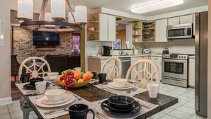 A modern kitchen with built-in appliances, a dining area with a wooden table set for four, and a brick fireplace.