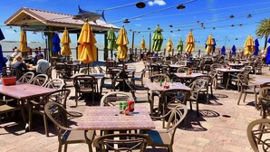 An outdoor dining area with tables and chairs, umbrellas, and a view of the sea.