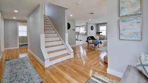 A spacious living area with a wooden staircase, a sofa set, and a dining area in the background.