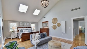 A bedroom with a bed, bedside tables, a dresser, a chandelier, and a large window.