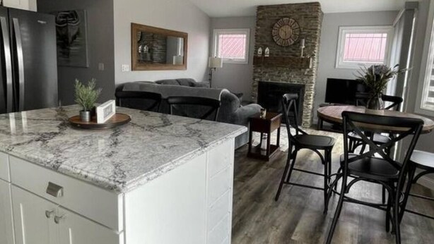 Een moderne keuken met een marmeren aanrecht, een stenen open haard en een eethoek met zwarte stoelen.