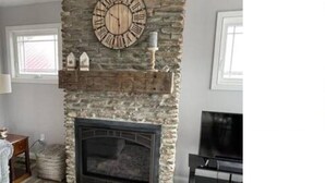 Een woonkamer met een stenen openhaard, een ronde wandklok en een televisie.
