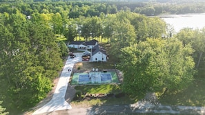Une vue aérienne d’une maison entourée d’arbres denses, avec un court de tennis situé dans le jardin avant.