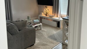 Un salon moderne avec un canapé gris, une table basse, un téléviseur à écran plat fixé au mur et une fenêtre avec des rideaux.