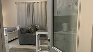 Une pièce avec un plancher en bois, un canapé gris, une table blanche et un ventilateur de plafond.