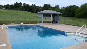Una piscina rectangular con borde de azulejos y un pequeño pabellón con techo al fondo.