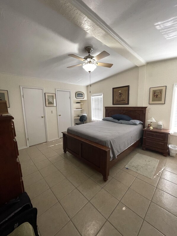 A bedroom with a bed, a nightstand, a dresser, a ceiling fan, and a window with blinds.