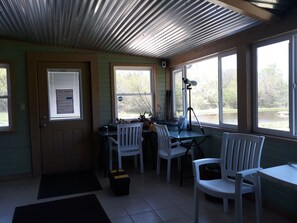 Ein Zimmer mit Schreibtisch, Stühlen, einem Teleskop und Fenstern mit Blick auf ein Gewässer.