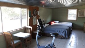 Una habitación con una cama, un escritorio, una silla, una bicicleta estática y un dardo.
