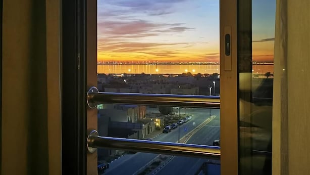 A view from a window with a metal railing, overlooking a cityscape at sunset with a bridge in the distance. - Tripper Inn (Dammam)