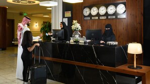 A hotel reception desk with a marble counter, multiple clocks displaying different city times, and a modern lamp. - Tripper Inn (Dammam)