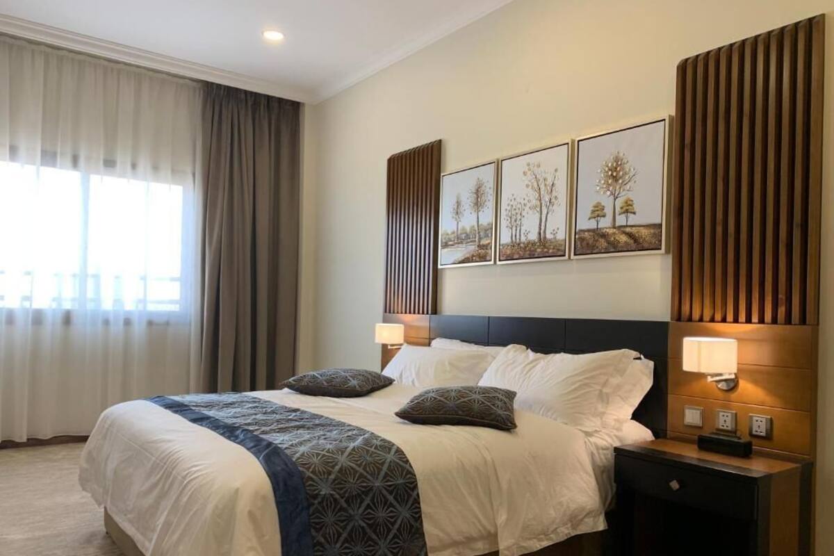A hotel room with a large bed, two bedside tables with lamps, a headboard, and three framed pictures on the wall.