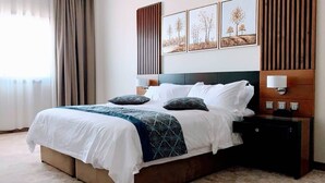 A neatly made bed with a white and blue patterned bedspread, two pillows, and a bedside table with a lamp. - Tripper Inn (Dammam)
