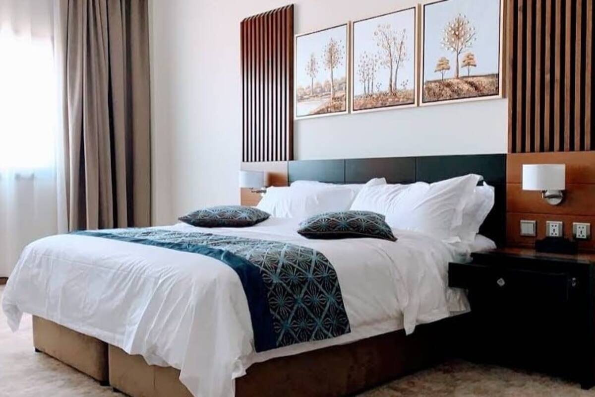 A neatly made bed with a white and blue patterned bedspread, two pillows, and a bedside table with a lamp.