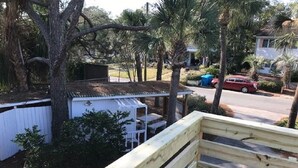 Un barrio residencial con una terraza de madera, un cobertizo blanco y un coche rojo estacionado en la calle.