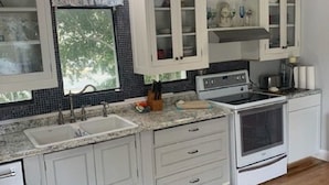 A kitchen with white cabinets, a double sink, a stove, and a window with a view of trees. -  Elevated Apt steps from beach. Furnished Parking Utilities, TV Internet Include (Tybee Island)