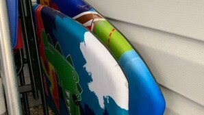 Un juego de cojines exteriores coloridos con motivos de tiburón apoyados contra una pared blanca.