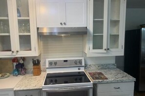 Una cocina con gabinetes blancos, extractor de acero inoxidable y encimera de granito.