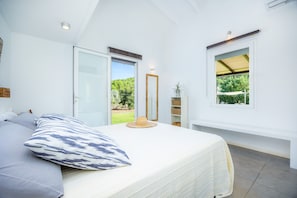 A bedroom with a bed, a large window, a mirror, and a view of greenery outside.