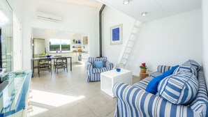 Ein modernes Wohnzimmer mit einer Couch, Sesseln, einem Couchtisch und einer Küche im Hintergrund.