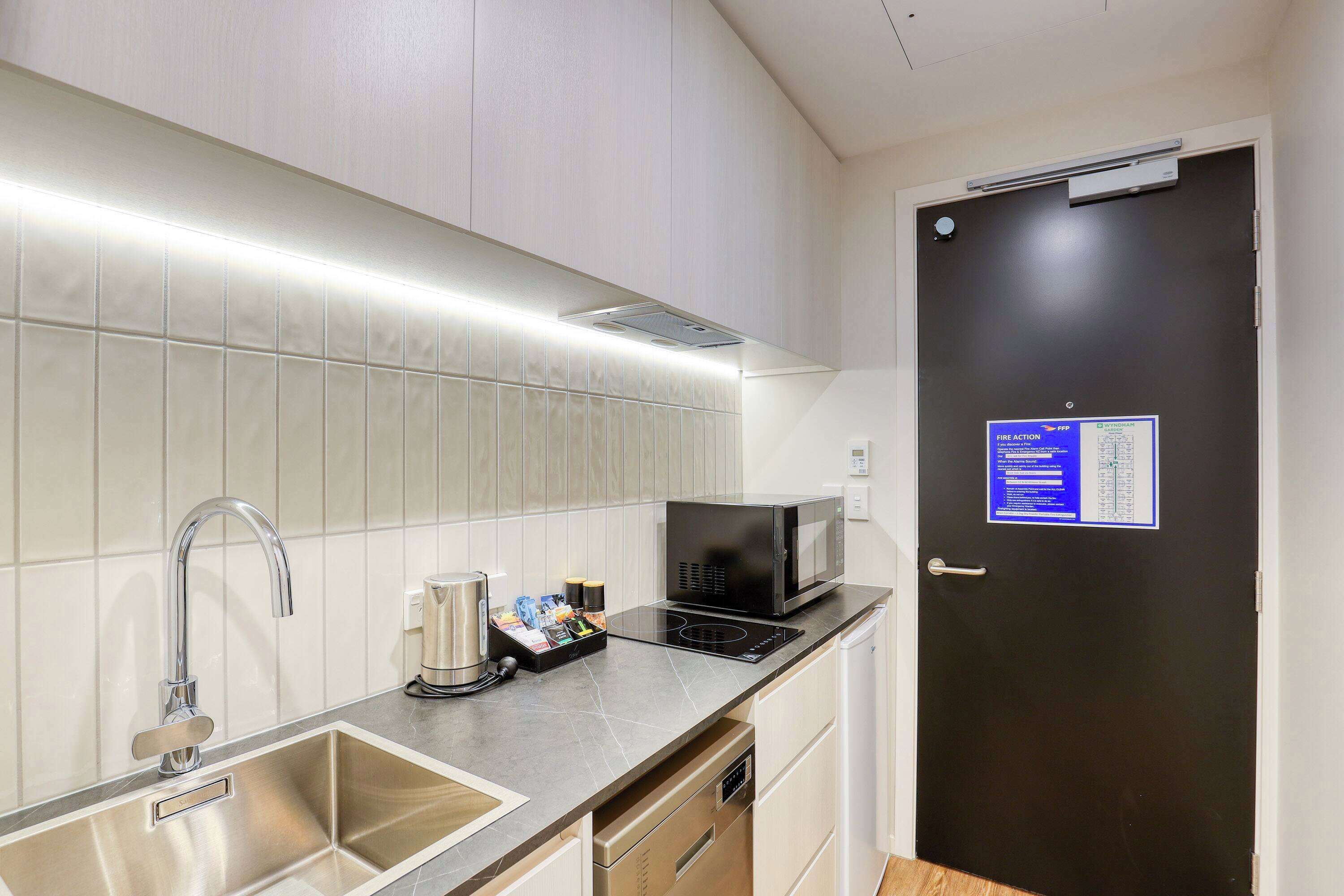 A compact kitchen with a stainless steel sink, a microwave, and a kettle on the countertop.