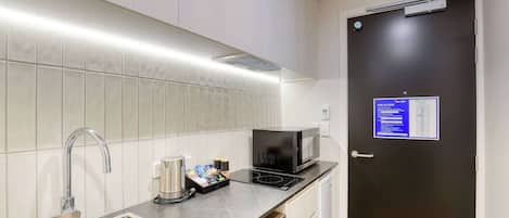 A compact kitchen with a stainless steel sink, a microwave, and a kettle on the countertop.