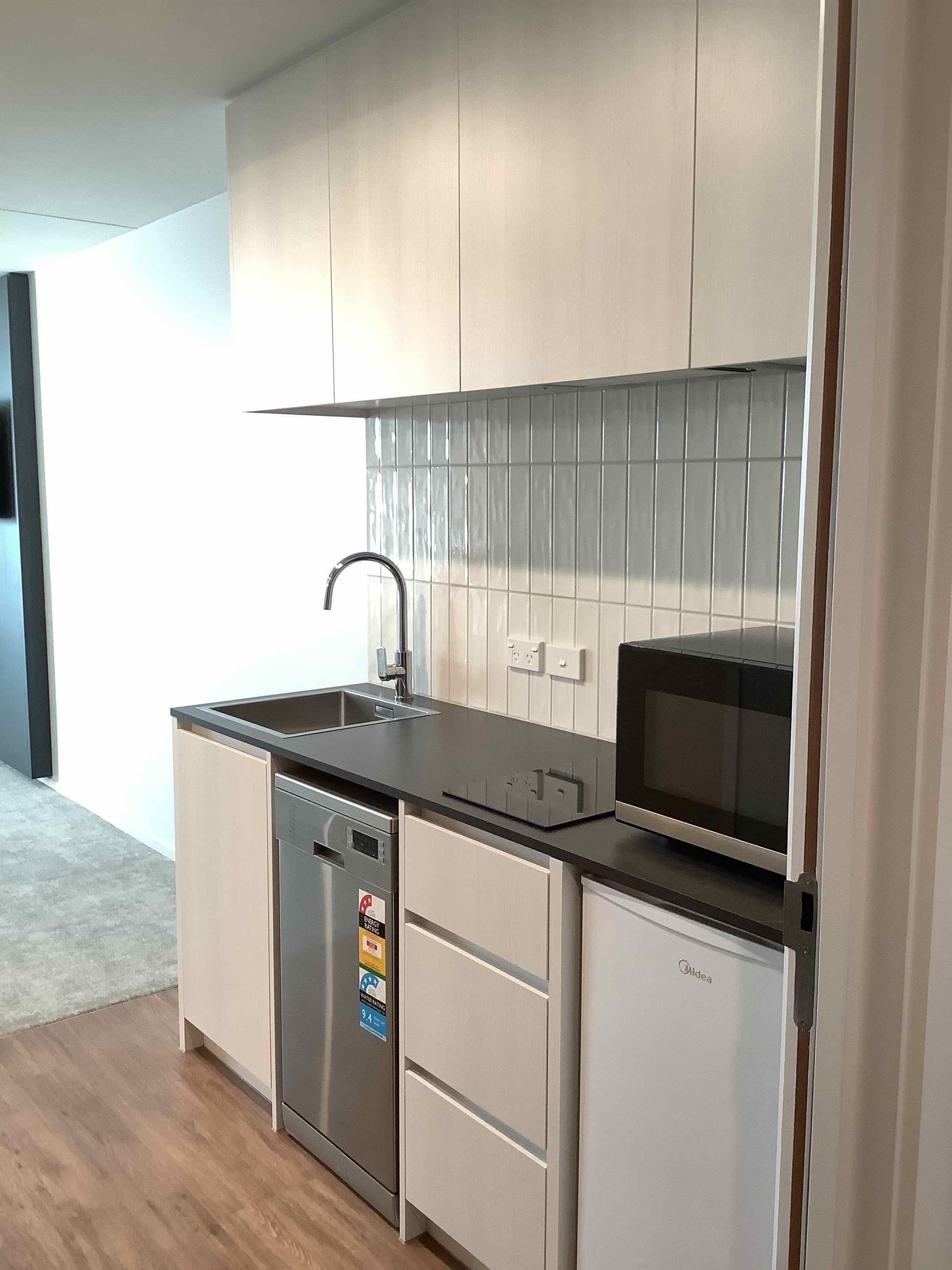 A modern kitchen with white cabinets, a stainless steel dishwasher, a microwave, and a sink with a faucet.