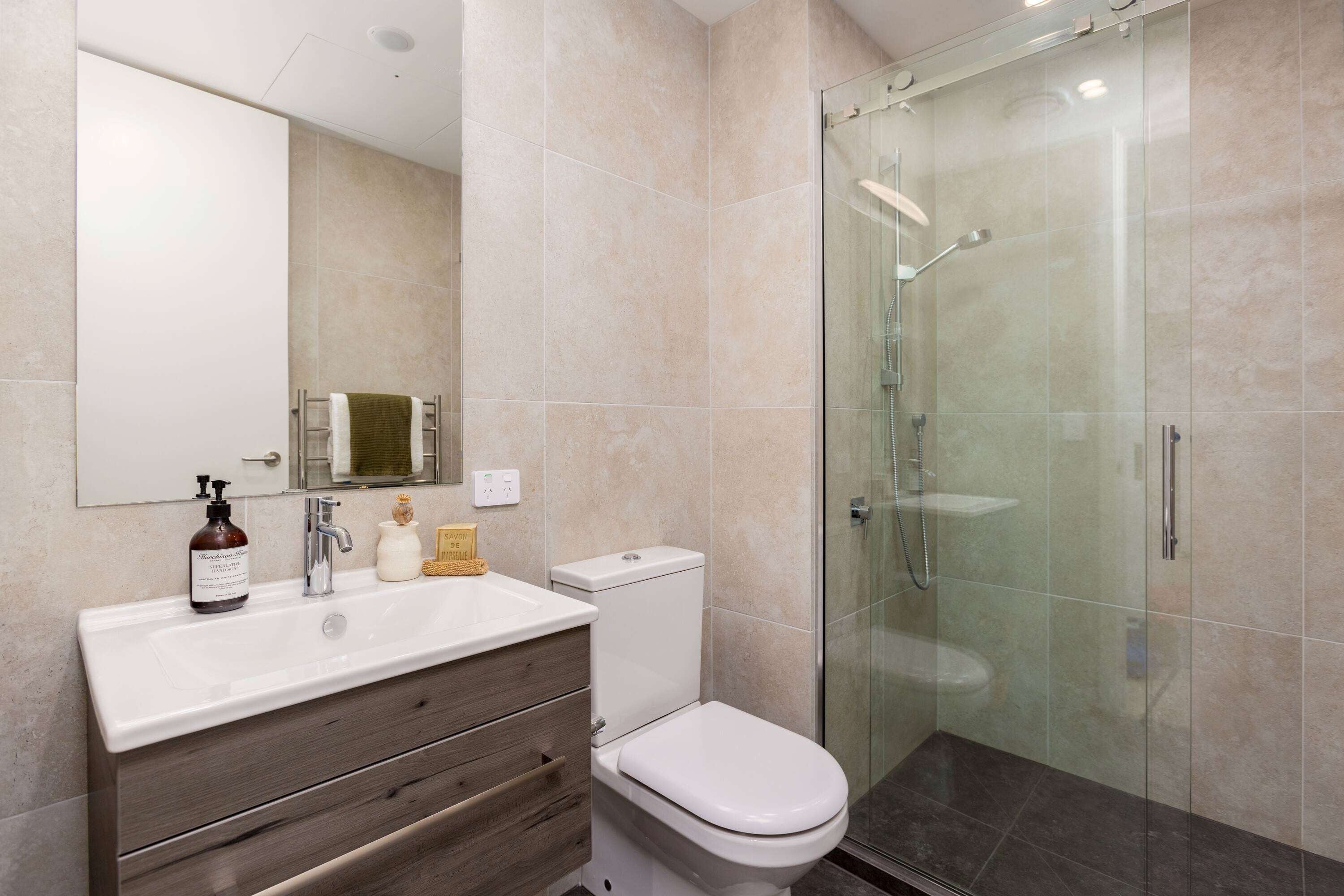 A modern bathroom with a glass-enclosed shower, a white sink with a wooden vanity, and a toilet.