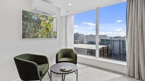 A modern room with a large window, two green armchairs, a small round table, and a large abstract painting. - Wyndham Garden Christchurch (Christchurch)