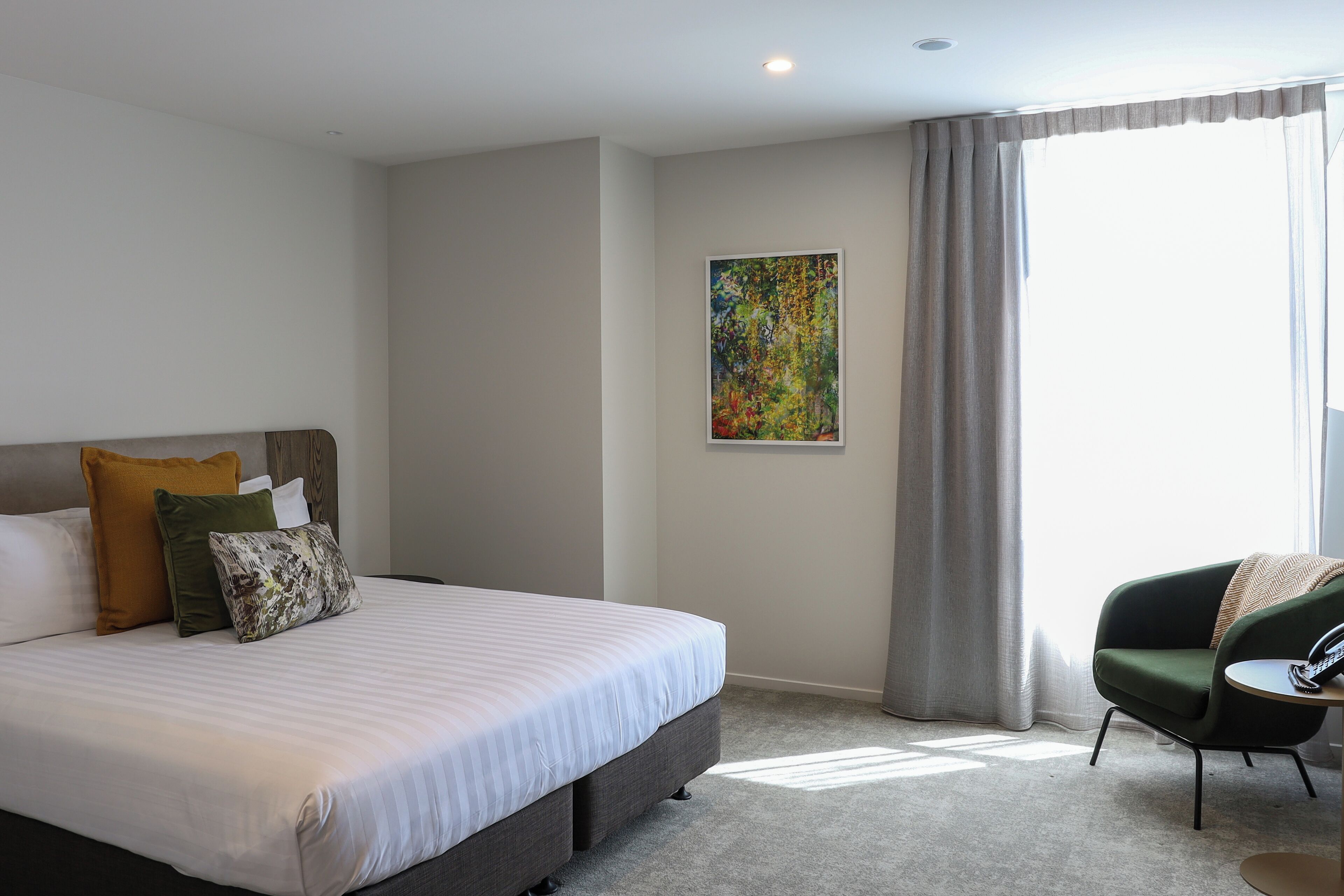 A hotel room with a large bed, a chair, a painting on the wall, and a window with curtains.