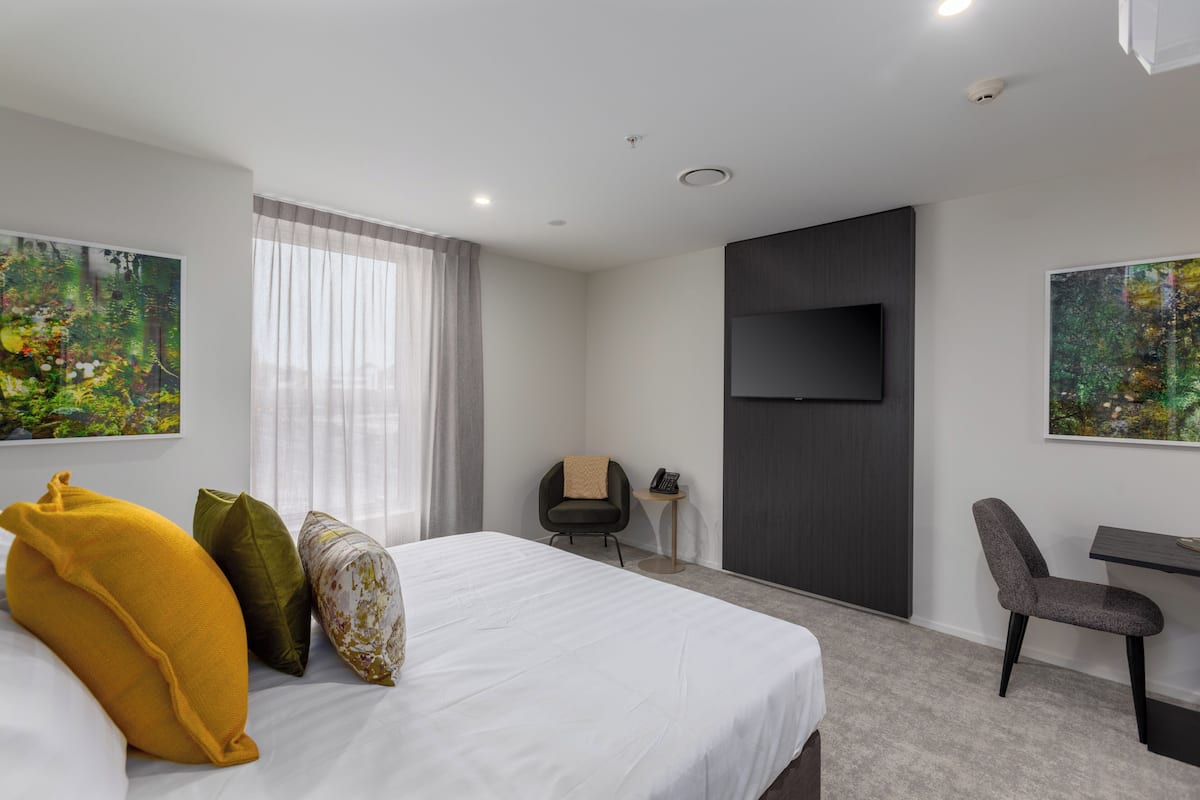A hotel room with a large bed, a desk, a chair, a TV, and two paintings on the walls.