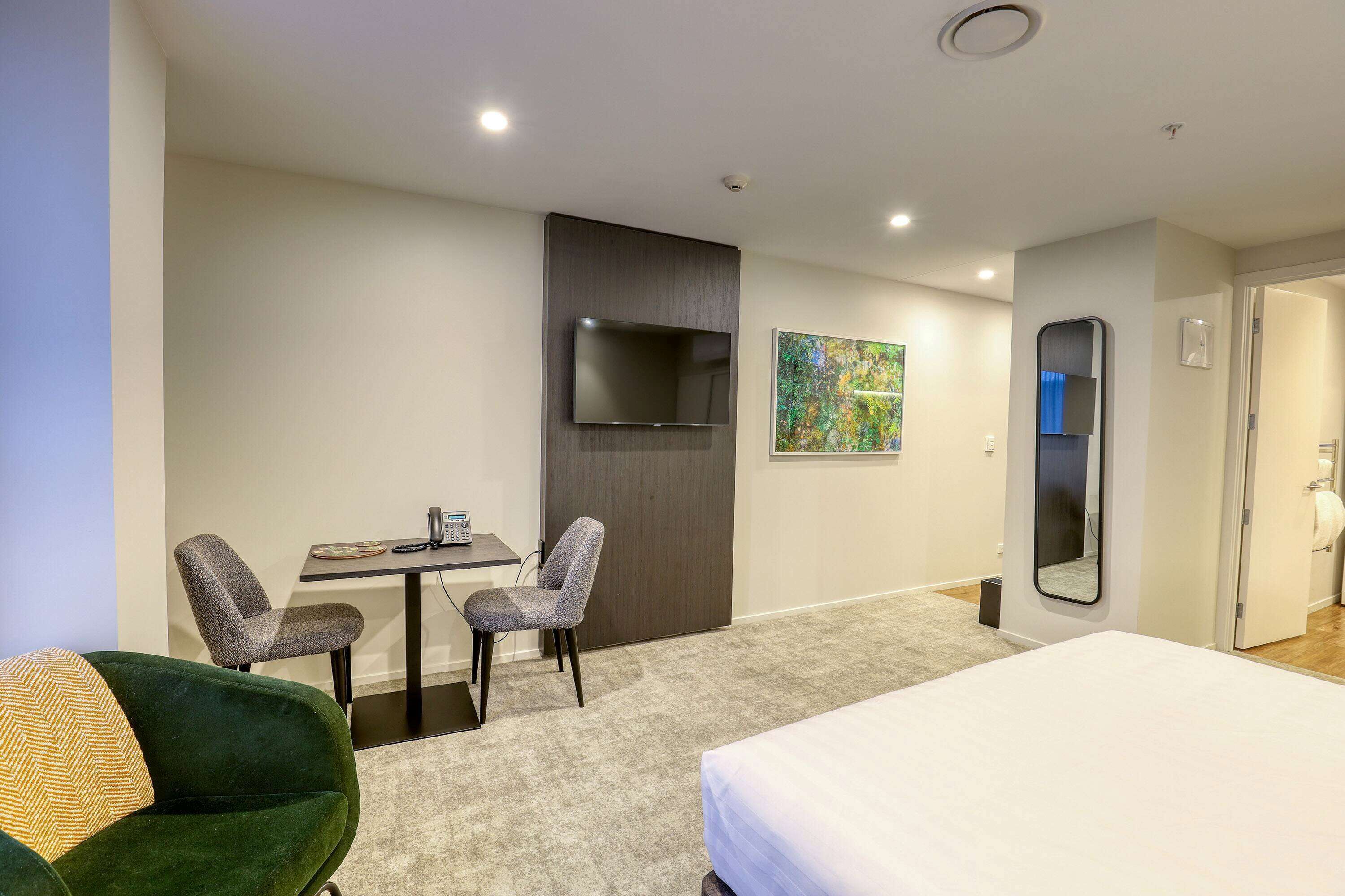 Une chambre d’hôtel avec un lit, deux chaises, un bureau, une télévision et un tableau au mur.