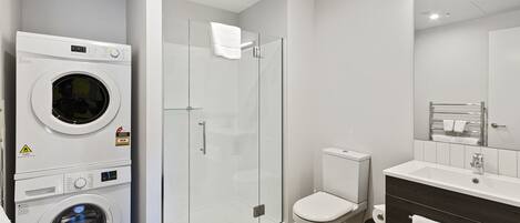 Een moderne badkamer met een douchecabine van glas, een toilet en een wasmachine.