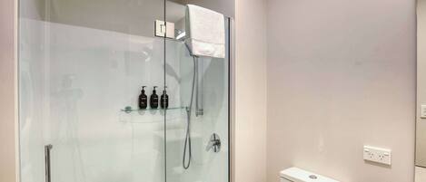 A modern bathroom with a glass-enclosed shower, a toilet, and a shelf with toiletries.