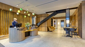 A reception area with a wooden reception desk, a staircase, and a seating area with a table and chairs. - Wyndham Garden Christchurch (Christchurch)