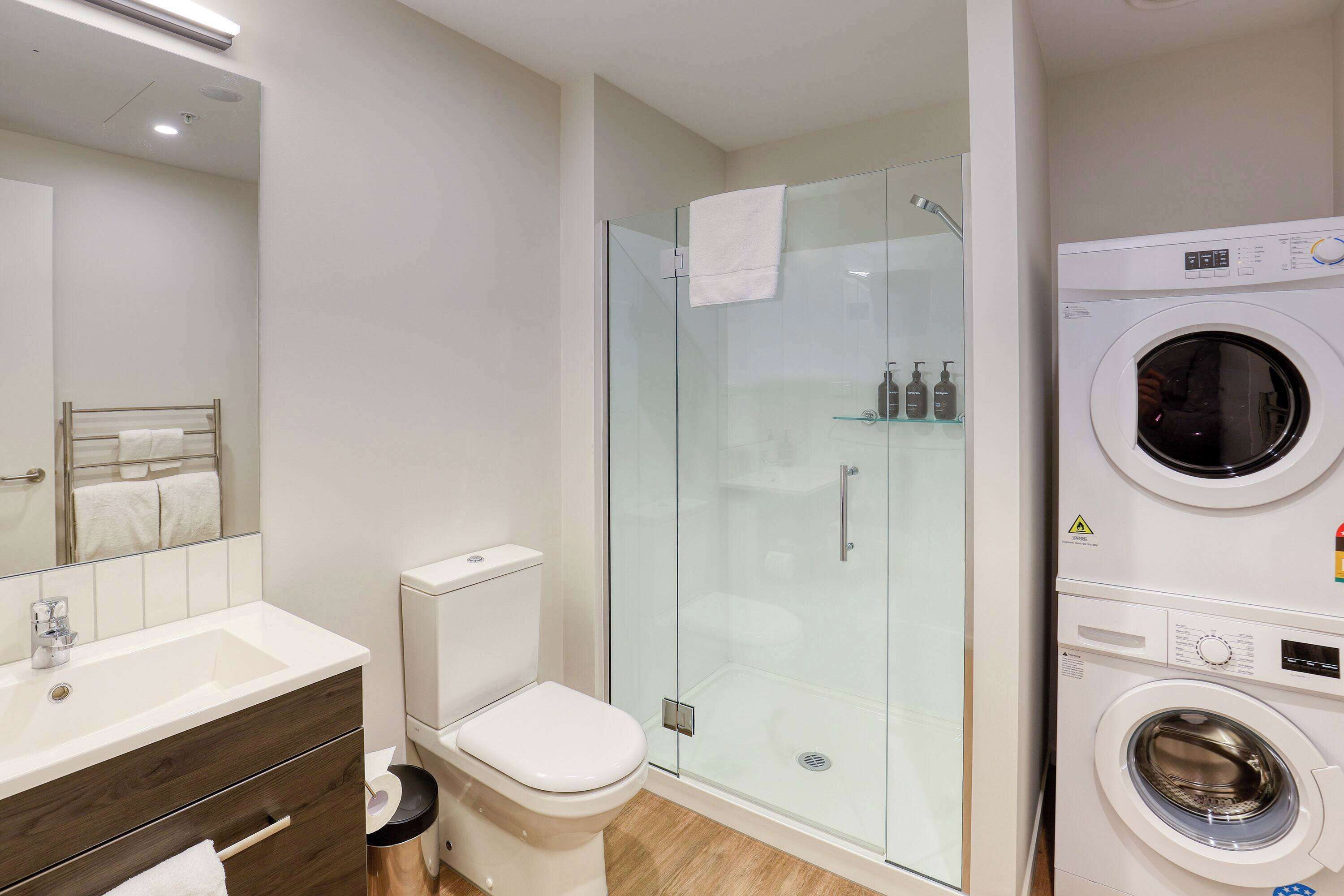A modern bathroom with a glass-enclosed shower, a white toilet, a sink with a mirror, and a front-loading washing machine.