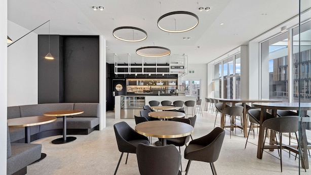 A modern interior with round tables and black chairs, a bar area, and large windows offering views. - Wyndham Garden Christchurch (Christchurch)