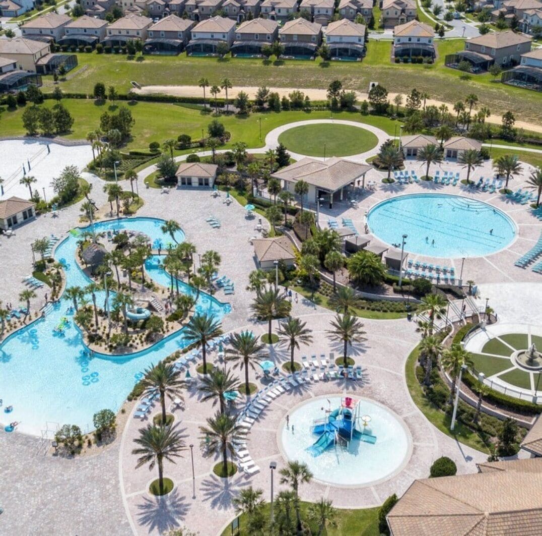 An aerial view of a resort with multiple swimming pools, palm trees, and a circular water feature.
