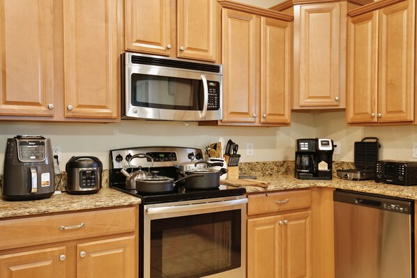 A kitchen with wooden cabinets, a stainless steel microwave, a stove, a coffee maker, and a toaster.