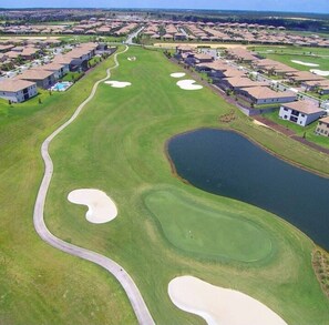 A golf course with bunkers, a pond, and residential buildings in the background.