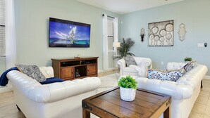 A living room with a white leather sofa, a wooden coffee table, and a television mounted on the wall. - Family vacation w/ Private Pool/Spa close to Disney,Parks & Golf (Champions gate)