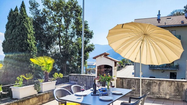 Une terrasse avec une table dressée pour deux personnes, un parasol jaune et des plantes en pot.