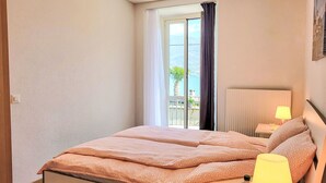 Une chambre à coucher avec un lit, une table de chevet, une lampe et une vue sur la mer par la fenêtre.