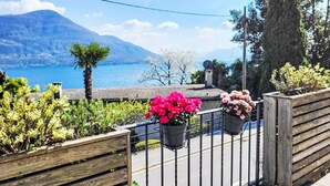 Un balcon agrémenté de plantes et de fleurs en pot, d’où l’on peut admirer un lac et des montagnes.