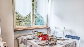 Un coin repas avec une table dressée pour deux personnes, une boîte de capsules de café Nespresso, une machine à café et un pichet en verre.