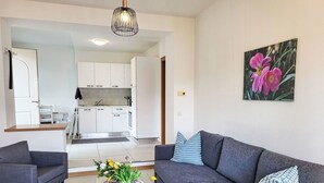 Un salon moderne avec un canapé gris, une table basse en verre et une cuisine en arrière-plan.