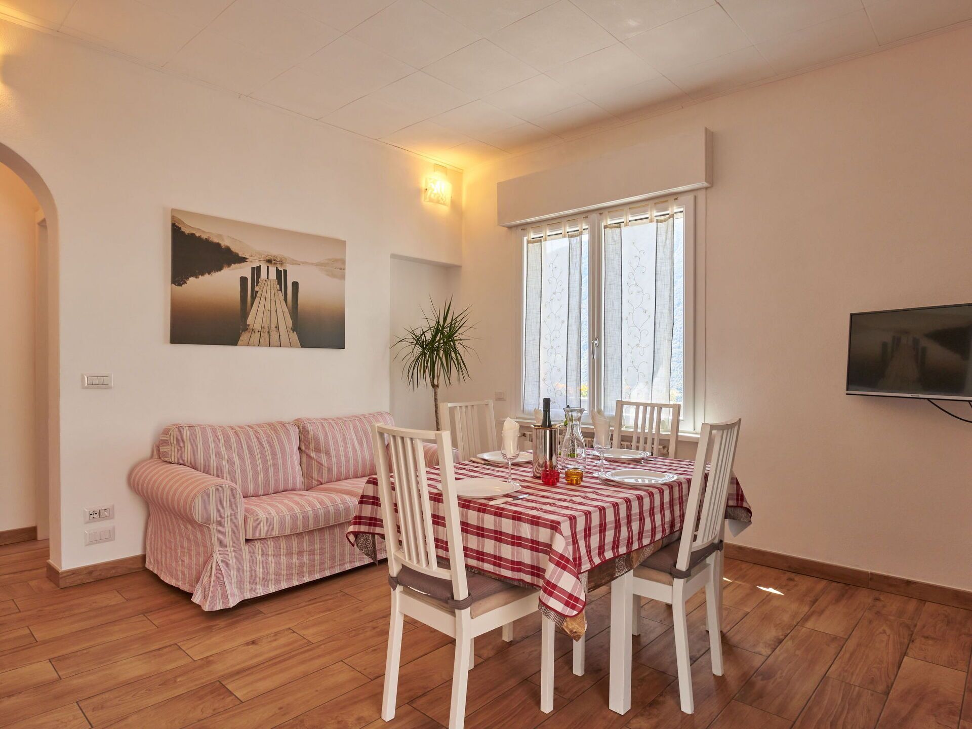 En matplats med ett bord för fyra personer, en soffa, en krukväxt och en tv som är monterad på väggen.