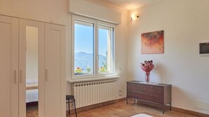 Une chambre avec une grande fenêtre, un plancher en bois, un radiateur, une commode et un tableau accroché au mur.